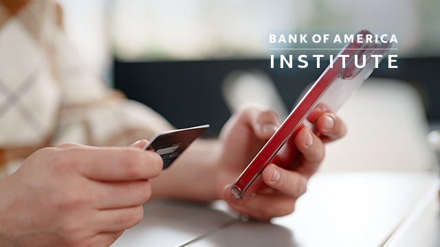 Close up to a hand holding a mobile phone and credit card.