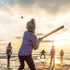 Family playing baseball on beach at sunset.